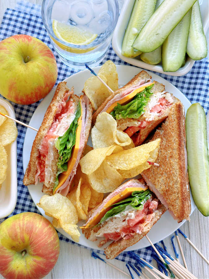 clubhouse sandwich plated with potato chips and dill pickles