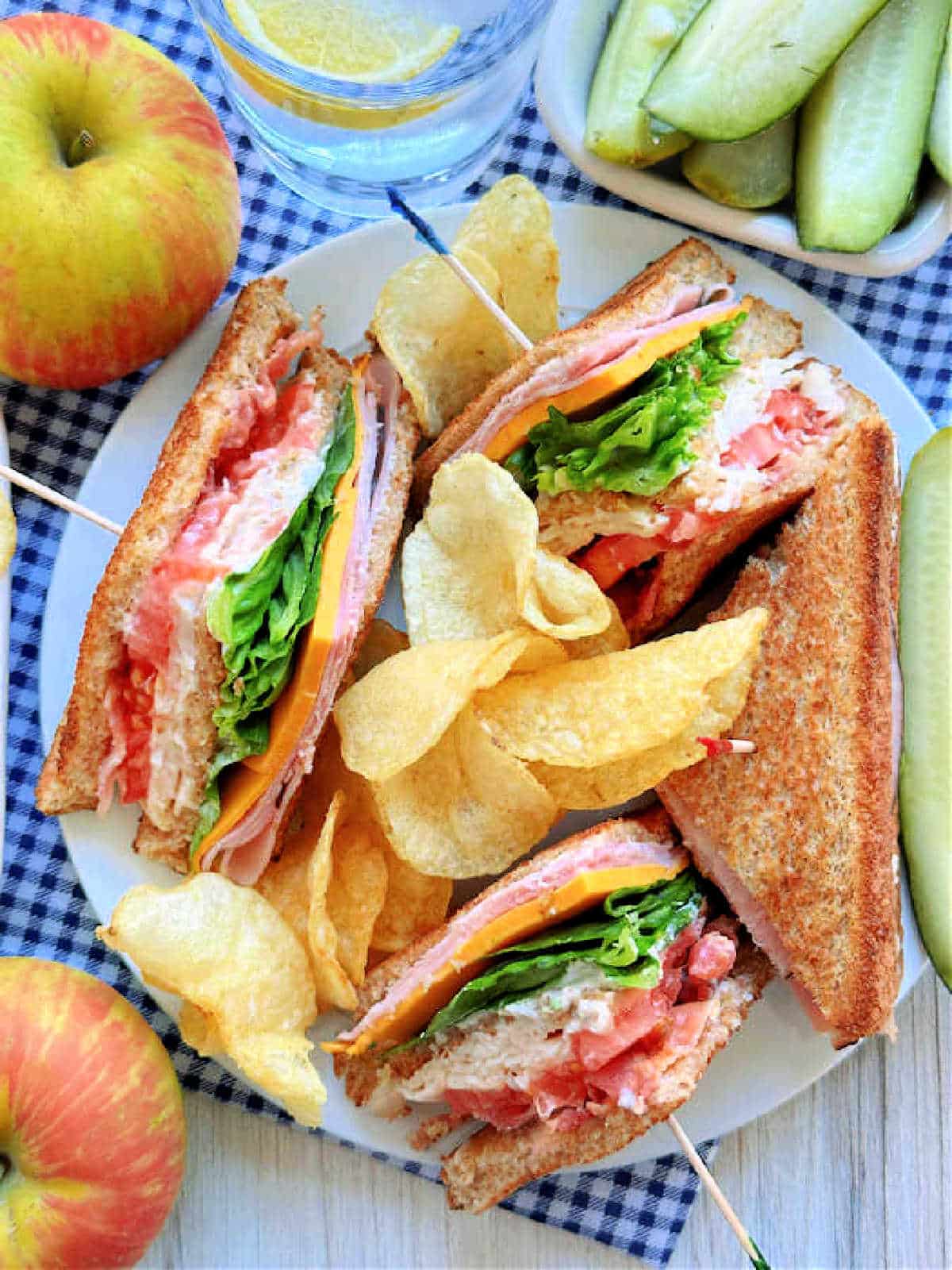 plated club sandwich with potato chips and pickle spears