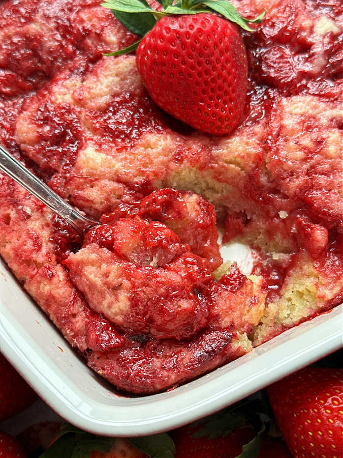serving a spoonful of strawberry spoon cake from the baking dish