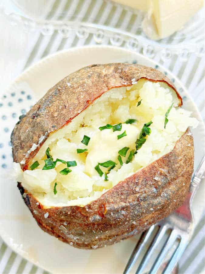 a perfectly cooked air fryer baked potato topped with butter and chives