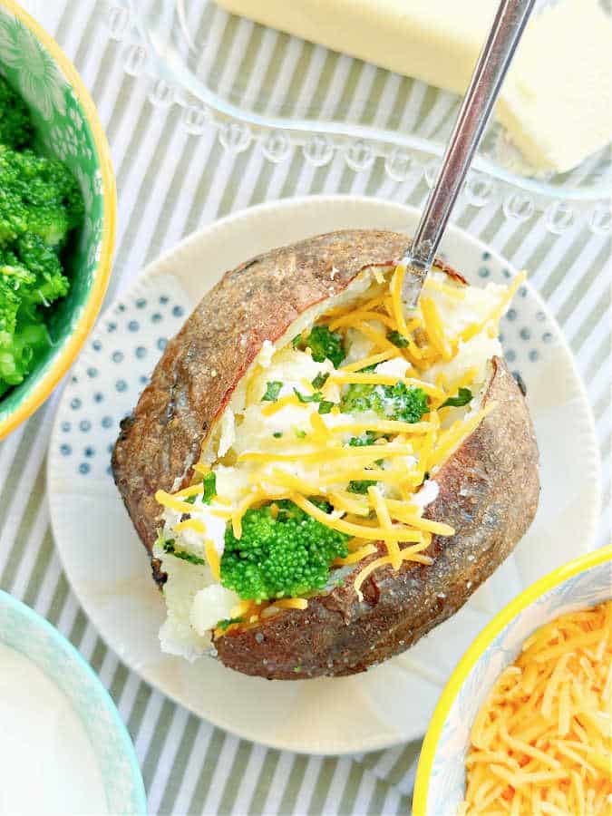 air fryer baked potato plated and topped with butter, sour cream, chives, broccoli and cheddar cheese
