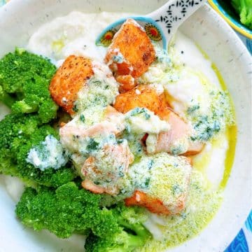air fryer salmon bites in a bowl served over mashed potatoes, with broccoli on the side and drizzled with a creamy garlic sauce
