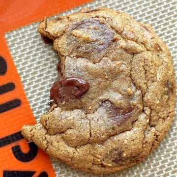 an espresso cookie with a bite taken out of it on a sheet pan lined with a silpat baking mat
