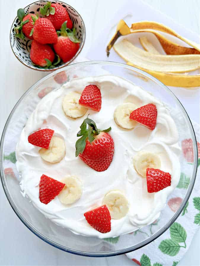 top view of strawberry banana pudding in trifle bowl topped with whipped cream and topped with sliced strawberries and bananas
