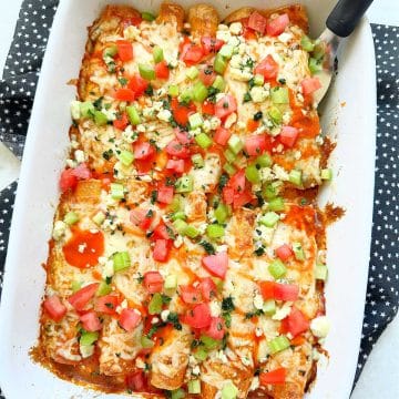buffalo chicken enchiladas in their baking dish garnished with fresh chopped tomatoes and celery