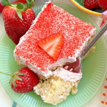 a piece of strawberry tres leches cake plated with fresh strawberries
