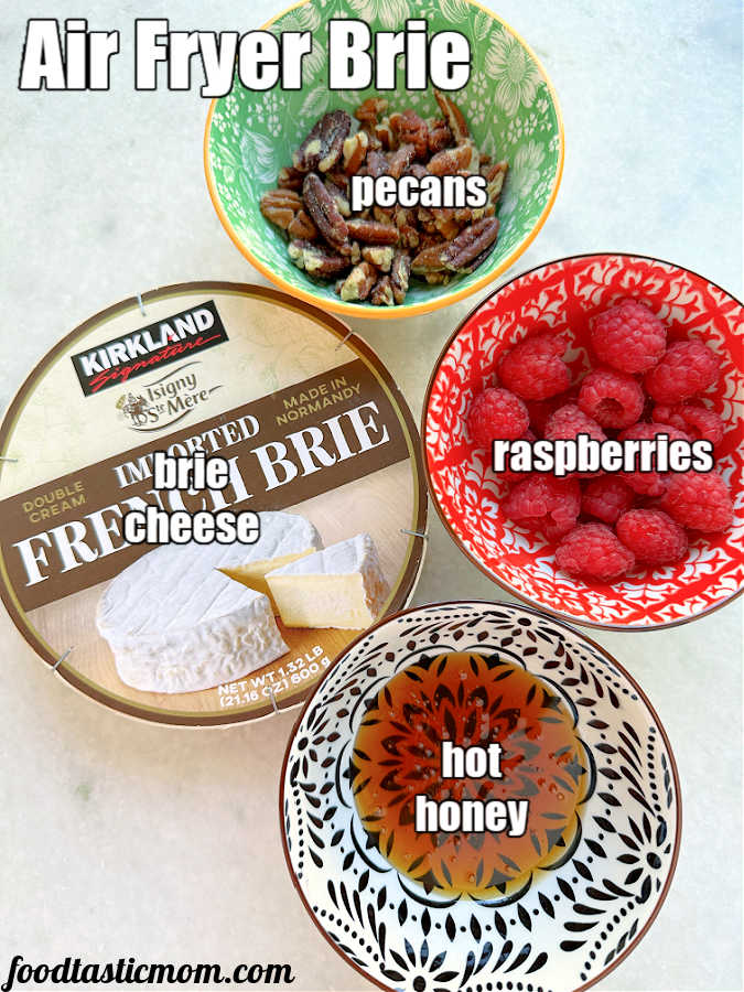 ingredients for making air fryer baked brie - brie cheese, pecans, hot honey and raspberries