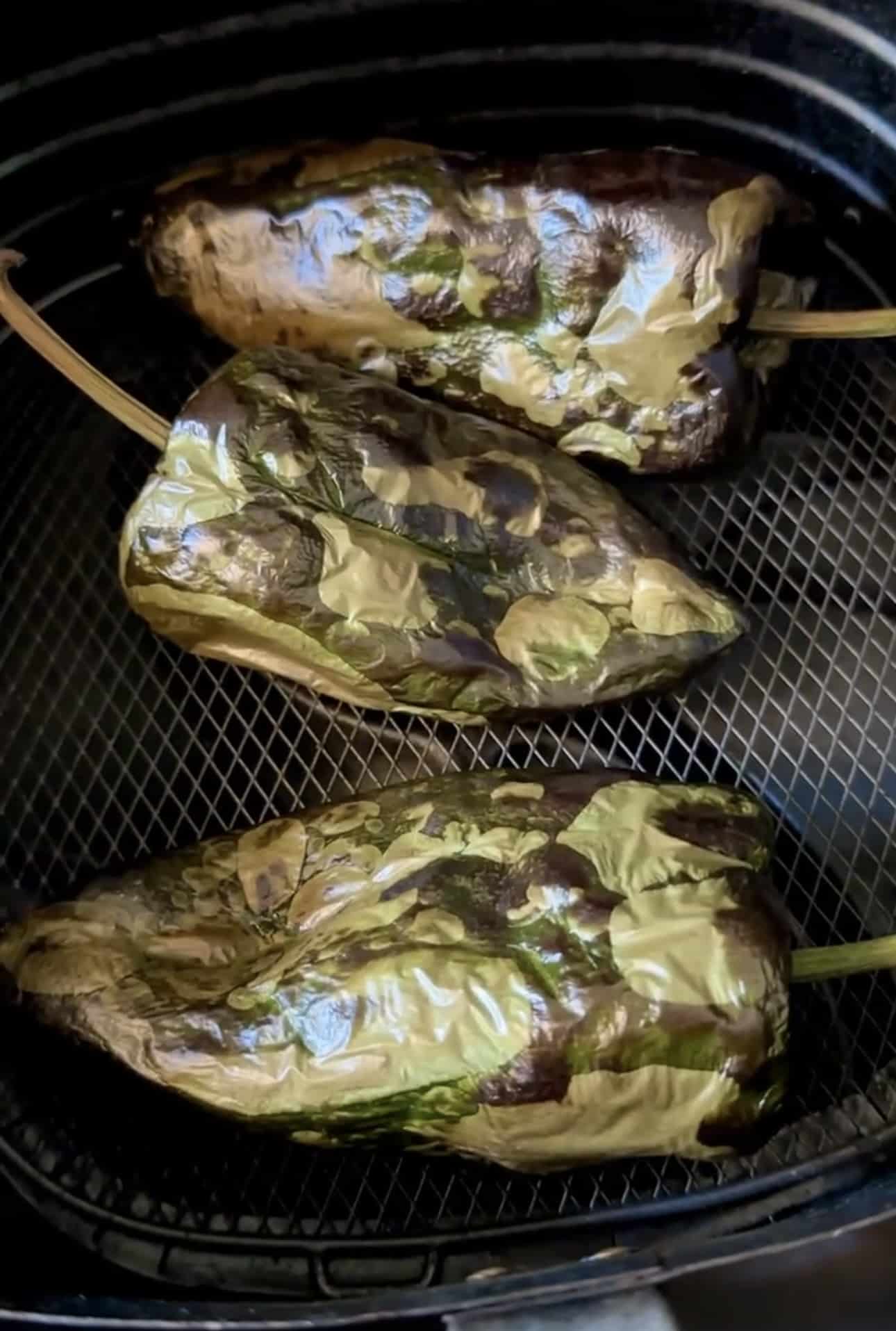 three roasted poblano peppers in the basket of an air fryer