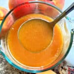 peach syrup being scooped from a bowl with a ladle