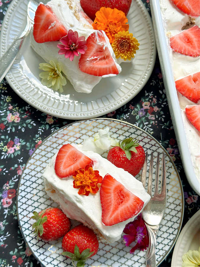 two slices of strawberry tiramisu on plates, garnished with fresh strawberries and edible flowers