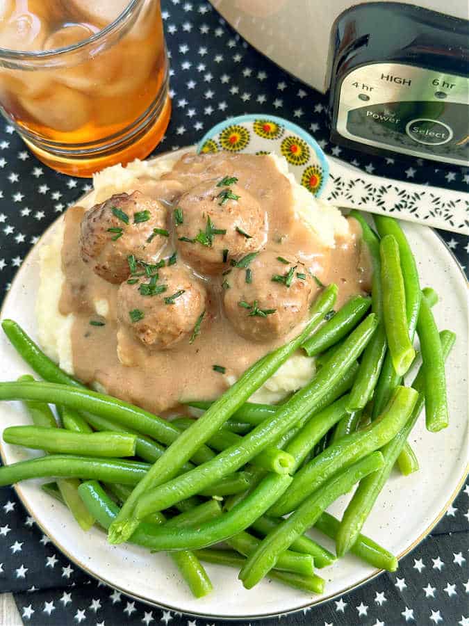 swedish meatballs and sauce plated with mashed potatoes and green beans