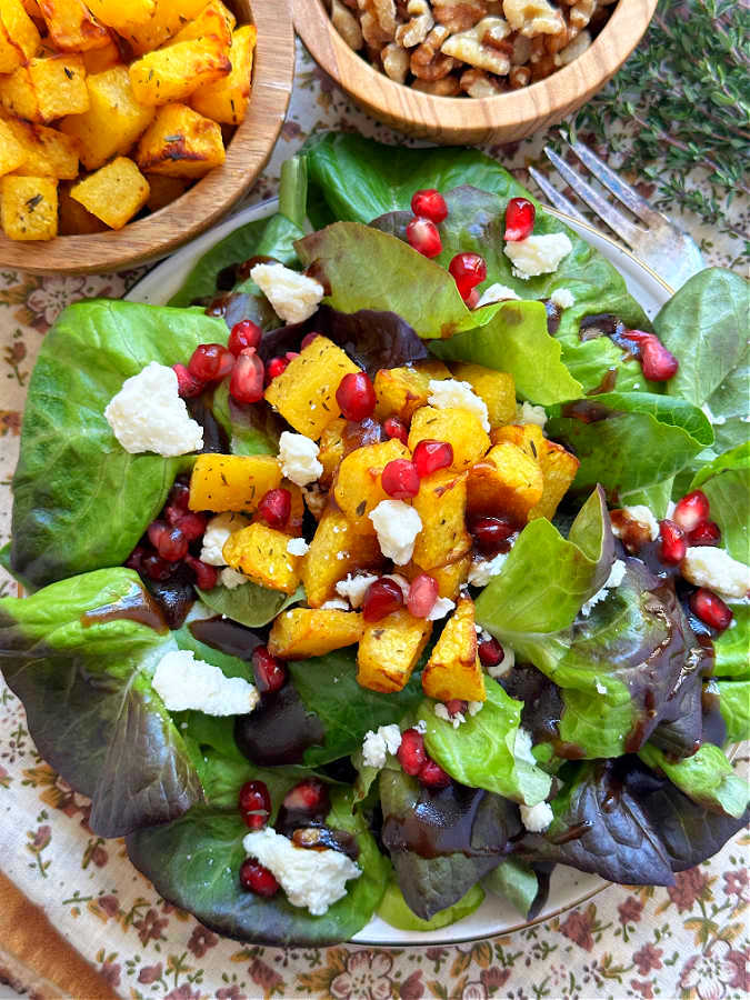 roast pumpkin salad on a plate, with extra pumpkin and walnuts on the side as garnish