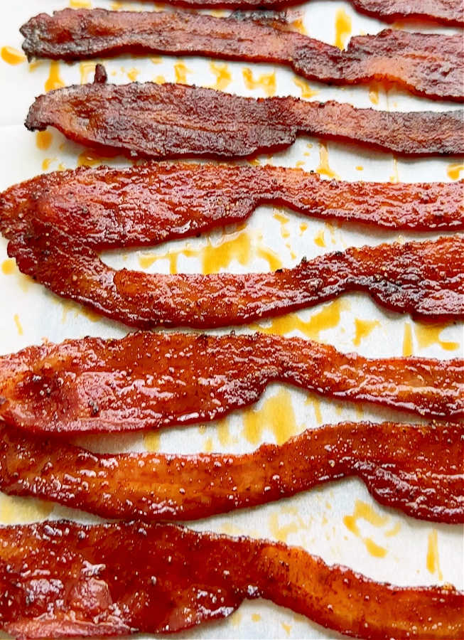 A close up picture of cooked slices of candied bacon just out of the oven and cooling on a piece of parchment paper.