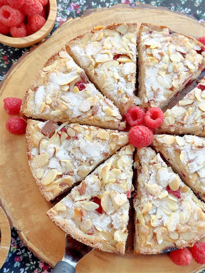 raspberry almond cake on a wooden cake platter, sliced and ready to serve