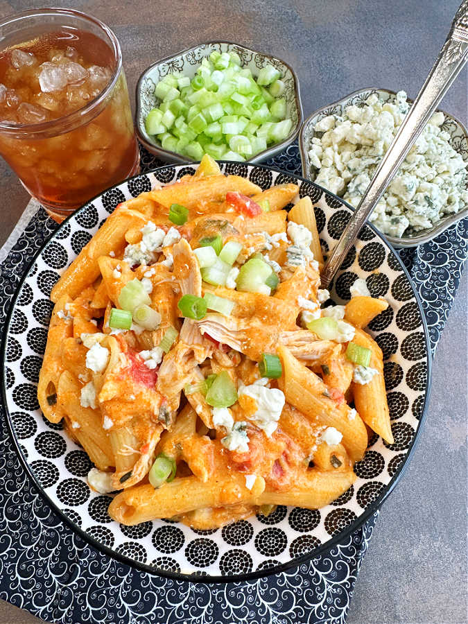 a bowlful of cheesy buffalo chicken pasta pictured with celery and blue cheese garnish plus a glass of iced tea
