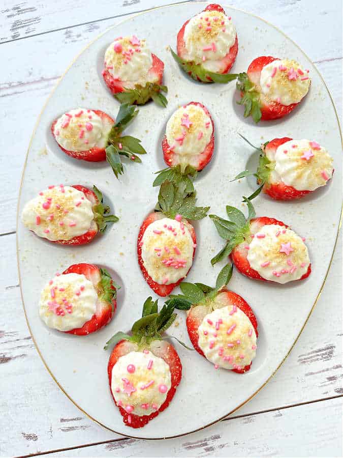 a plate full of deviled strawberries garnished with graham cracker crumbs and pink sprinkles