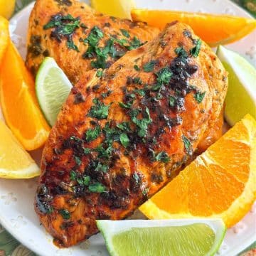 two perfectly cooked chicken breasts, marinated in citrus marinade. Plated and surrounded by slices of orange, lemon and lime.