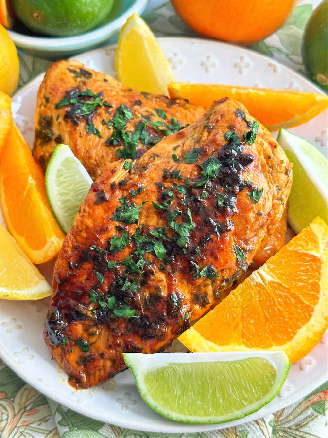 two citrus marinated chicken breasts plated with slices of orange, lemon and lime