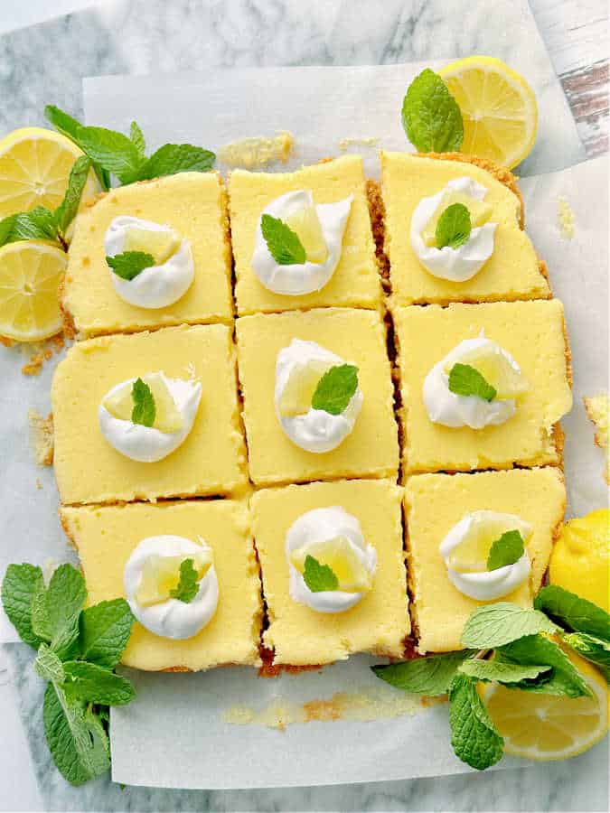 A pan of chilled lemon bars on parchment paper, cut into squares and ready to serve.
