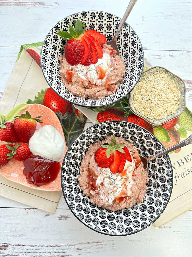 overhead shot of two bowls of strawberry oats, both garnished with fresh strawberries, yogurt and jam
