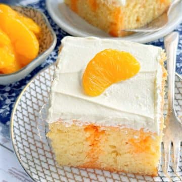 a slice of orange jello cake topped with vanilla cool whip frosting and a mandarin orange slice