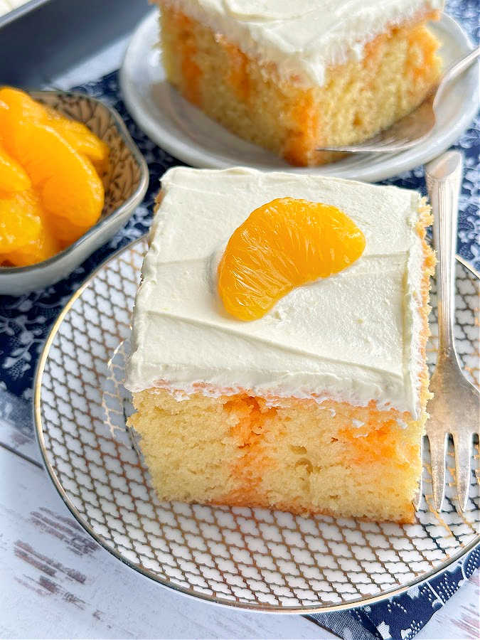 a slice of orange and vanilla jello cake plated and topped with a mandarin orange