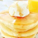 a stack of fluffy buttermilk pancakes crowned with a scoop of butter and maple syrup