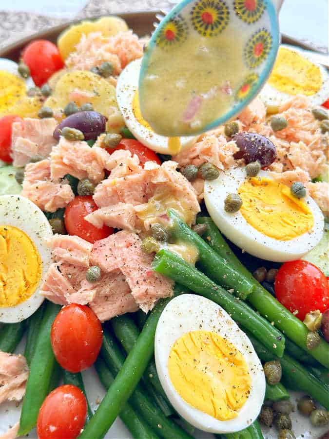 drizzling the lemony dressing over the nicoise salad