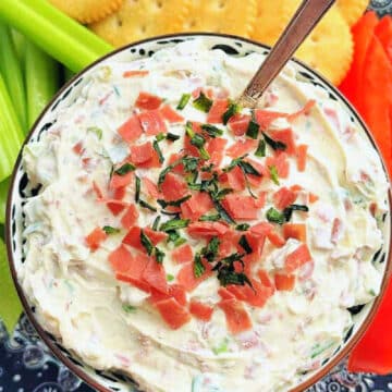 a bowl of dried beef dip garnished with chives and surrounded by crackers, celery and red pepper strips
