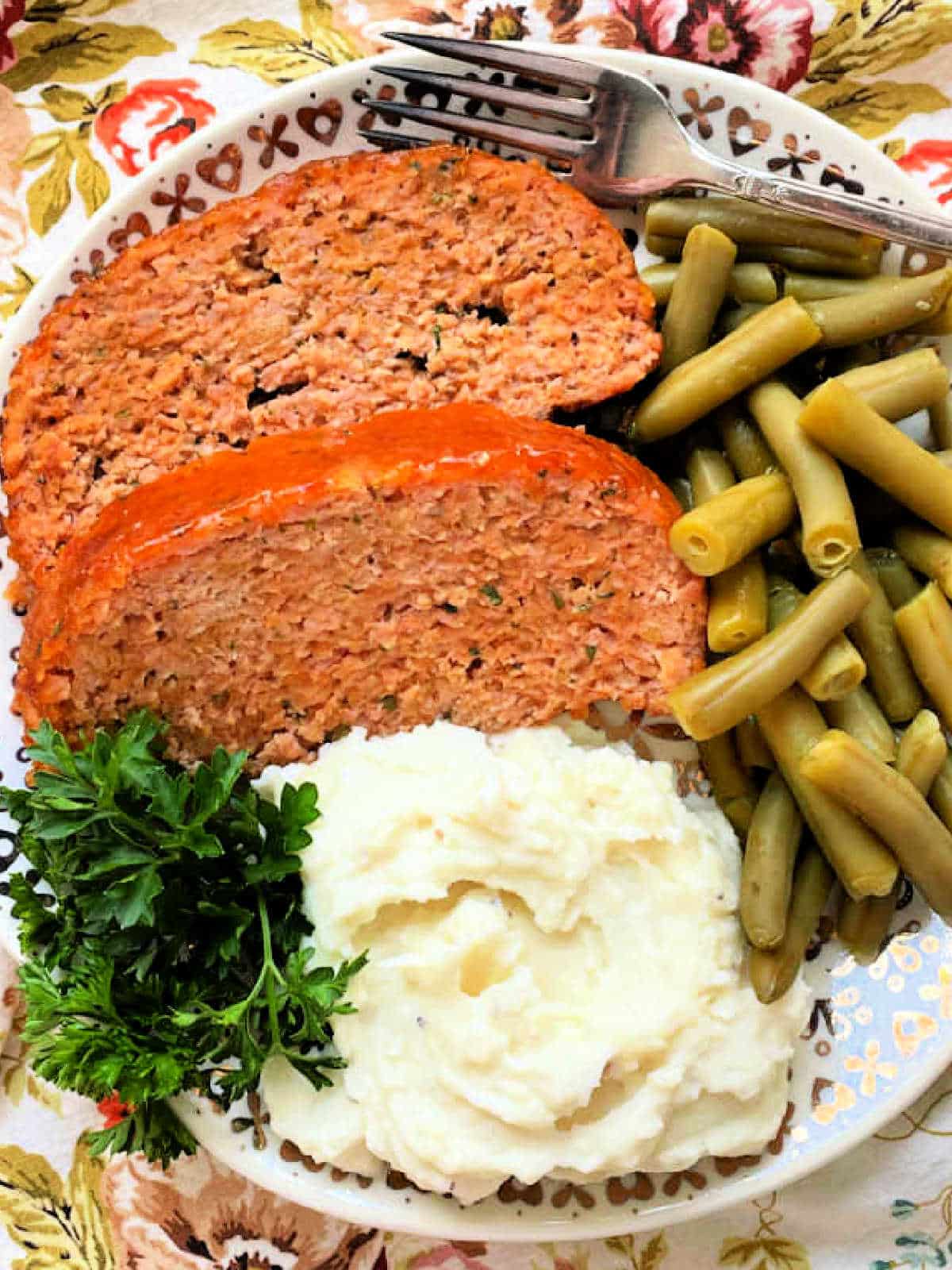 two slices of apricot glazed ham loaf plated with mashed potatoes and green beans