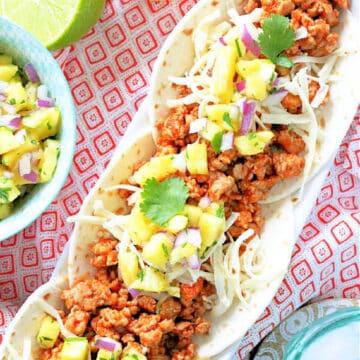 three plated pork tacos topped with fresh pineapple salsa