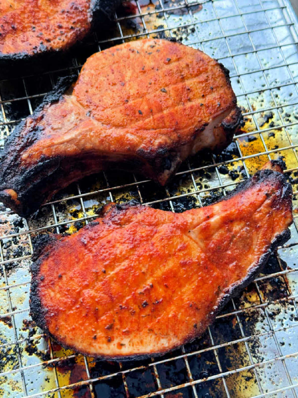 closer up photo of three broiled pork chops on a cooking rack set on top of a foil lined baking sheet