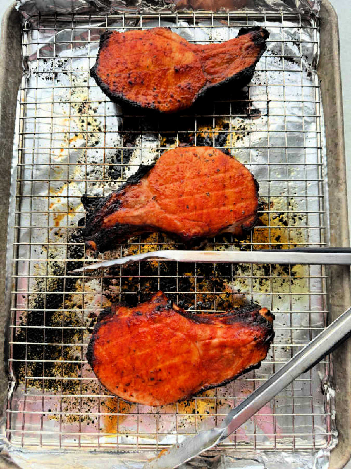 freshly broiled pork chops shown on a foil lined baking sheet