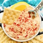 a bowl full of smoked tuna dip garnished with paprika and lemon slice with saltine crackers for dipping
