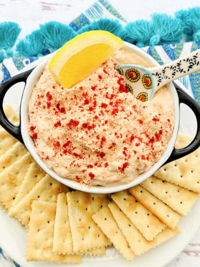 a bowl of smoked tuna dip garnished with paprika and lemon with saltine crackers for dipping