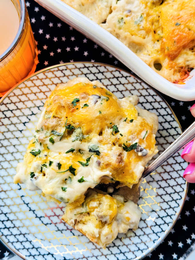 a slice of biscuits and gravy casserole served on a small plate with a glass of orange juice on the side