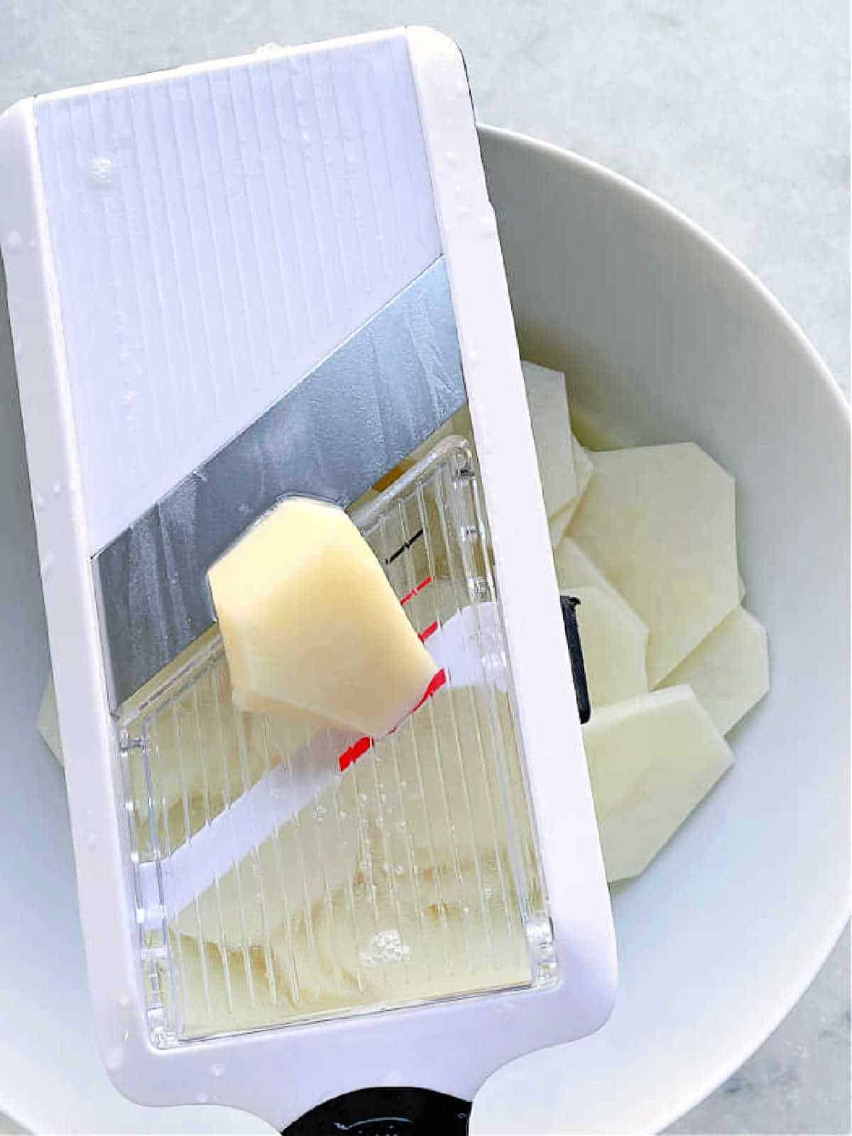 showing potatoes being sliced with a hand-held mandoline