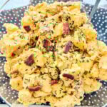 a clear plastic serving bowl full of freshly made loaded potato salad topped with crumbled bacon