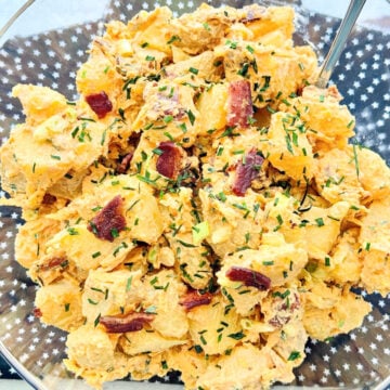 a clear plastic serving bowl full of freshly made loaded potato salad topped with crumbled bacon