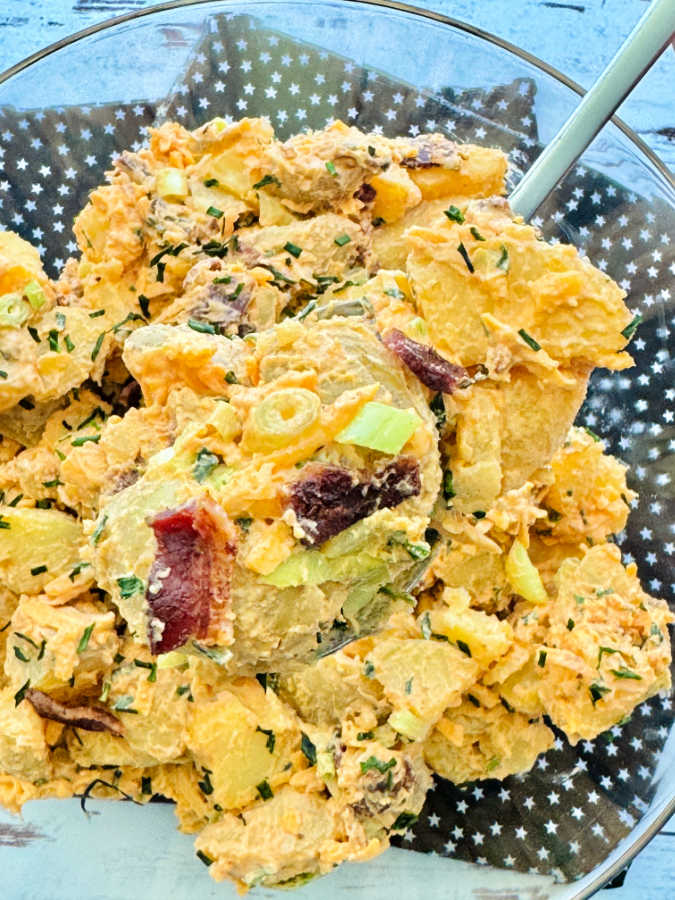 close up of a serving spoon scooping out some loaded potato salad from the serving bowl