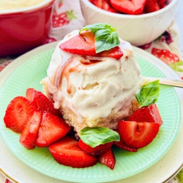 a slice of shortcake topped with vanilla gelato and balsamic strawberries, garnished with tiny fresh basil leaves
