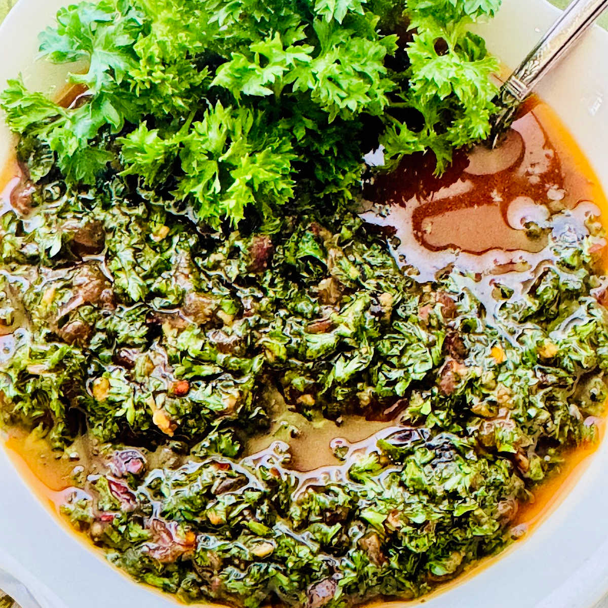 vibrant green fresh chimichurri sauce in a while bowl and garnished with more fresh parsley