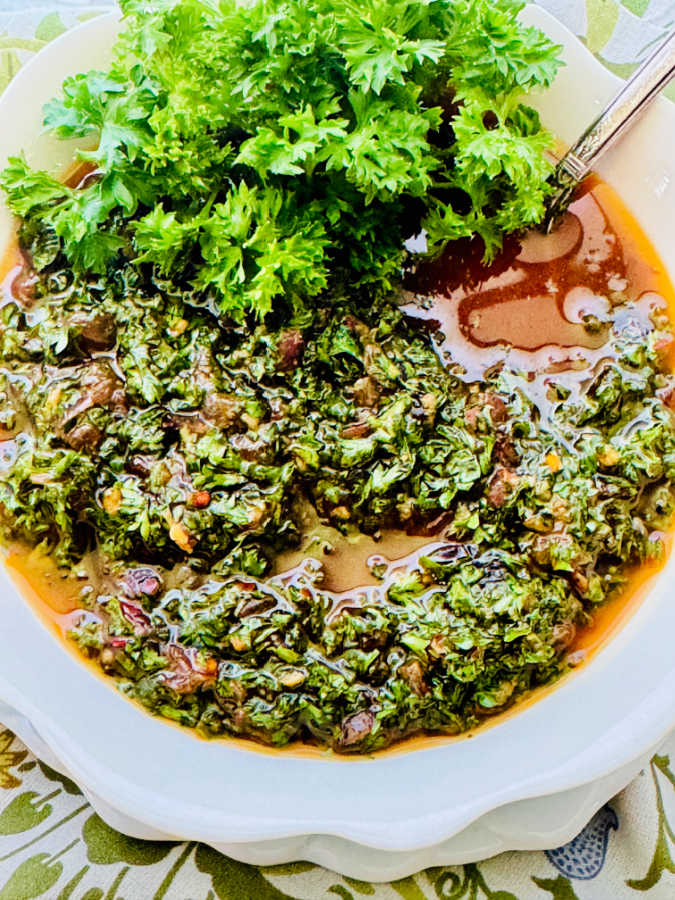 fresh made chimichuri sauce in a white bowl garnished with more fresh parsley