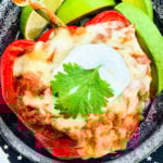 a taco stuffed red bell pepper plated with fresh avocado and lime slices