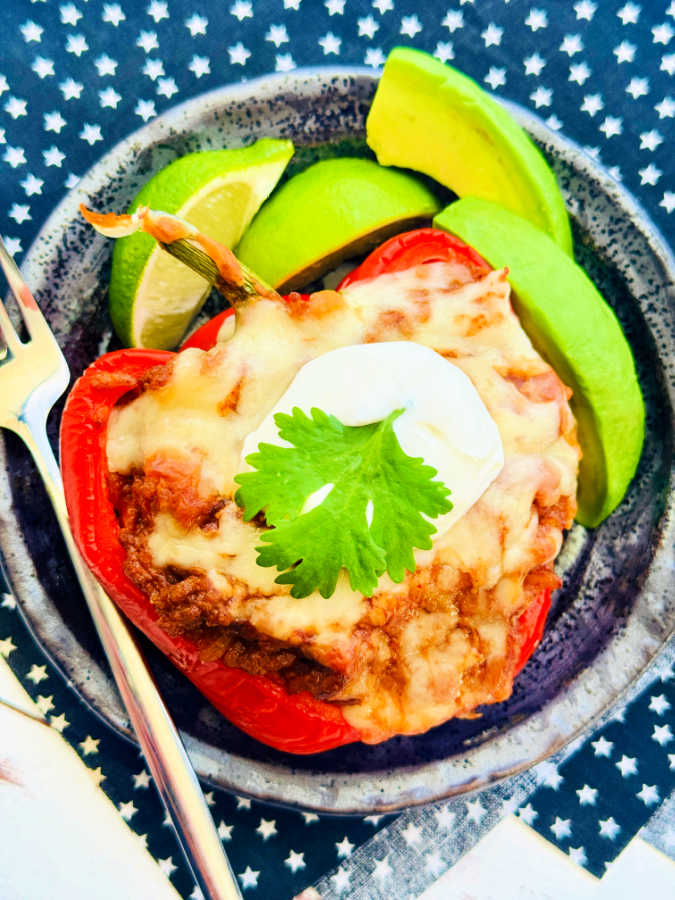 a taco stuffed pepper plated with sliced avocados and limes