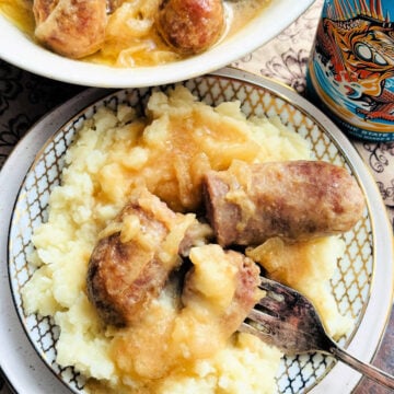a slow cooker beer brat plated with mashed potatoes and smothered in onions and gravy