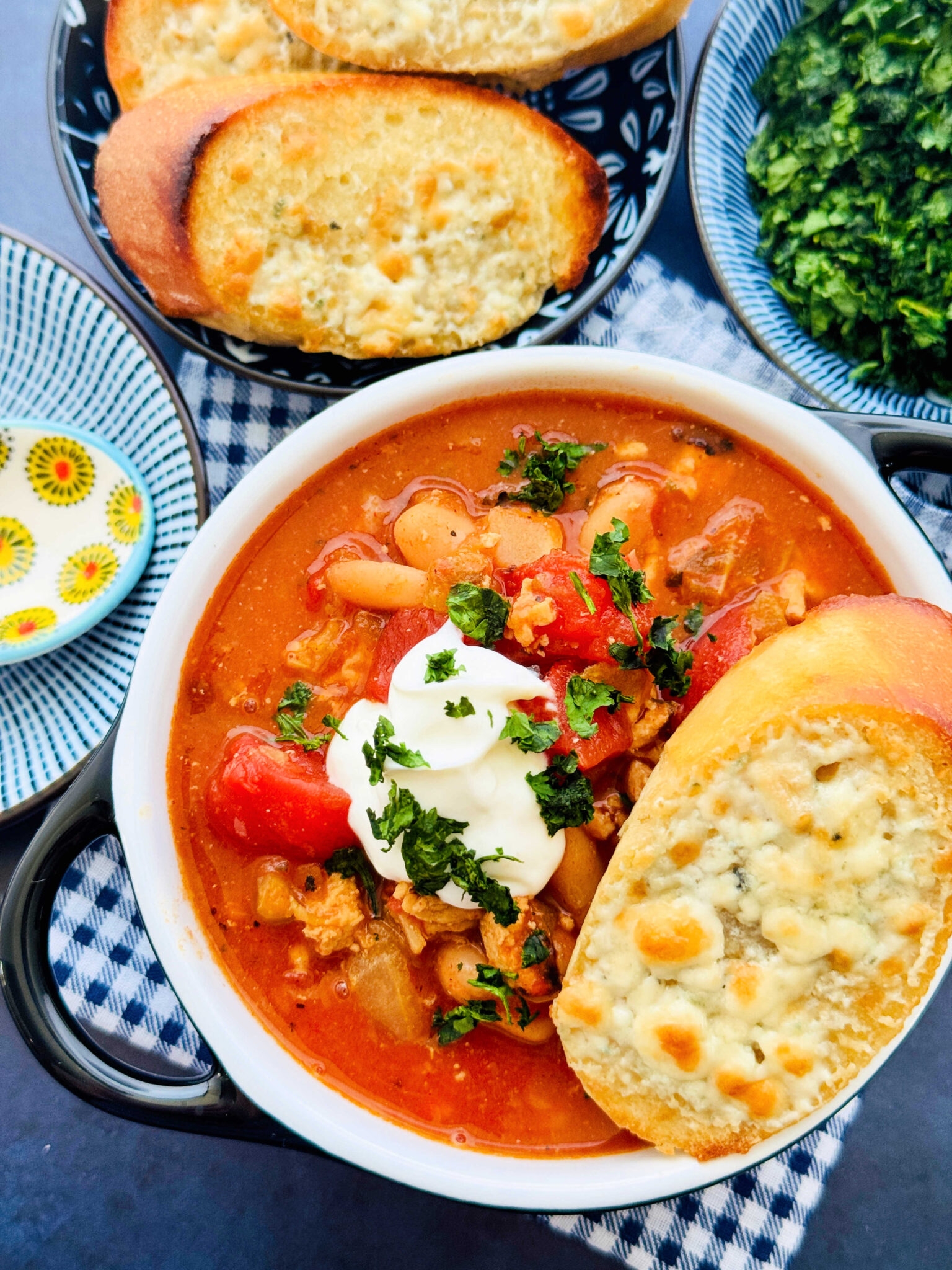 a bowl of buffalo chicken chili garnished with sour cream and a plate of blue cheese toast on the side