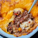 overhead view of cottage pie in baking dish with a spoonful taken out so that you can see the ground beef filling