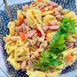 a clear glass bowl filled with tortellini pasta salad and garnished with fresh parsley