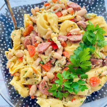 a clear glass bowl filled with tortellini pasta salad and garnished with fresh parsley